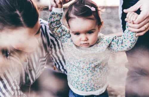 Kinderbetreuung in Zeiten von Corona-Pandemie Kleines Mädchen an den Händen der Eltern lernt laufen